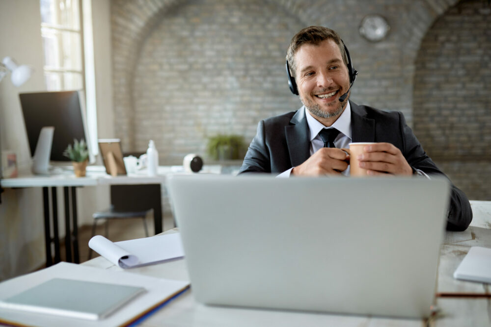 Happy businessman drinking coffee while having video call in the